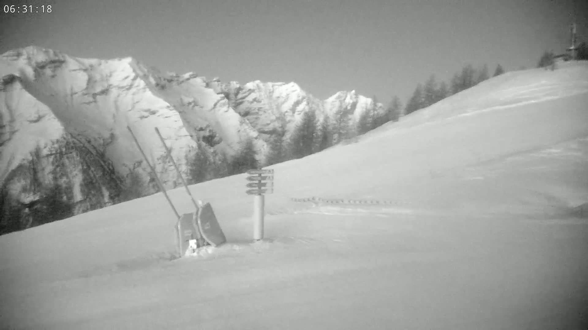 A snow-covered hillside with a snow-covered mountain in the background, a signpost, and two sleds leaning against a post.