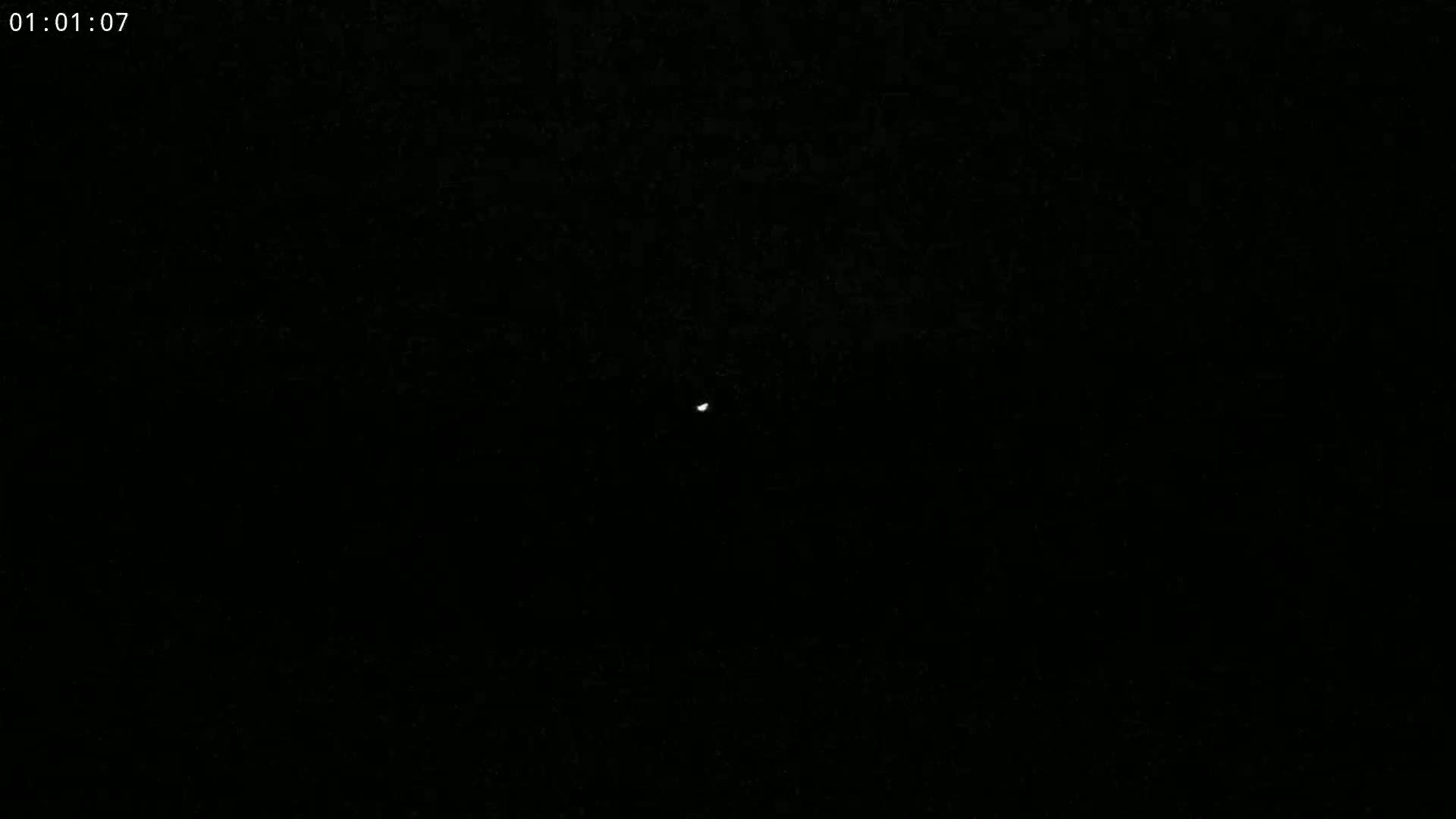 A small, bright light is visible in the center of a completely dark, nighttime sky.
