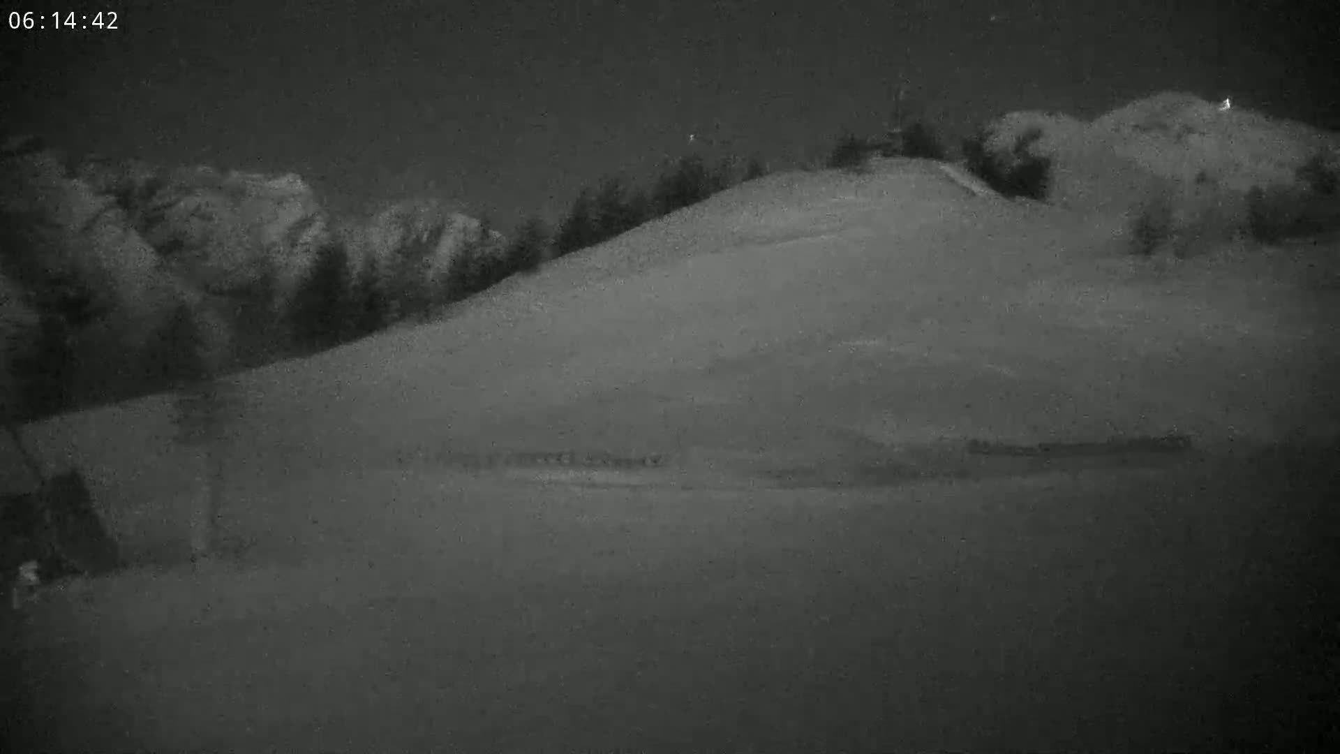 A snow-covered hill is seen at night, with a dark forest in the background under a dark sky.