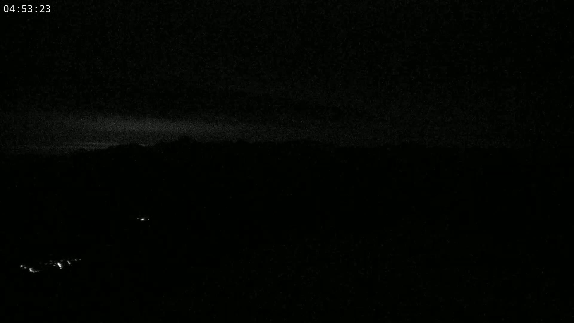 A nighttime, low-light view shows a dark landscape with a few faint lights visible in the distance.