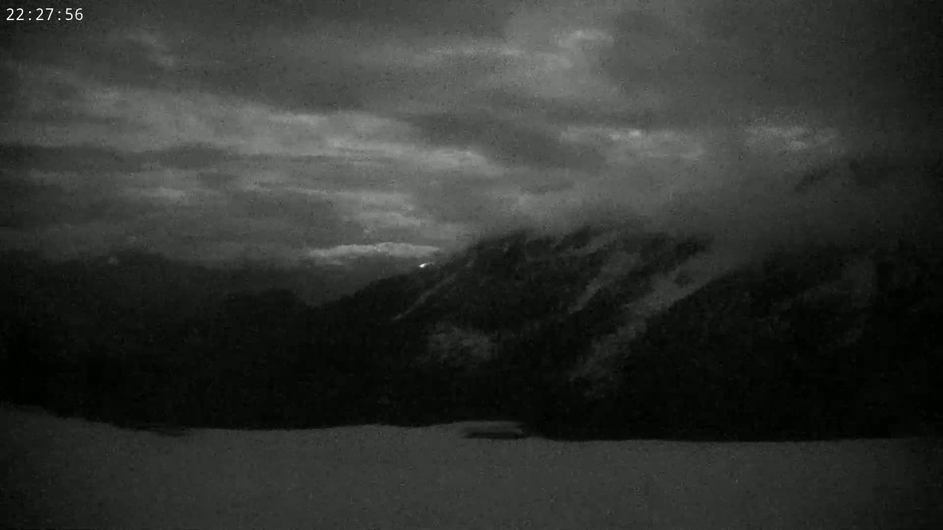 A dark, cloudy night scene shows a snow-covered landscape with mountains in the background.