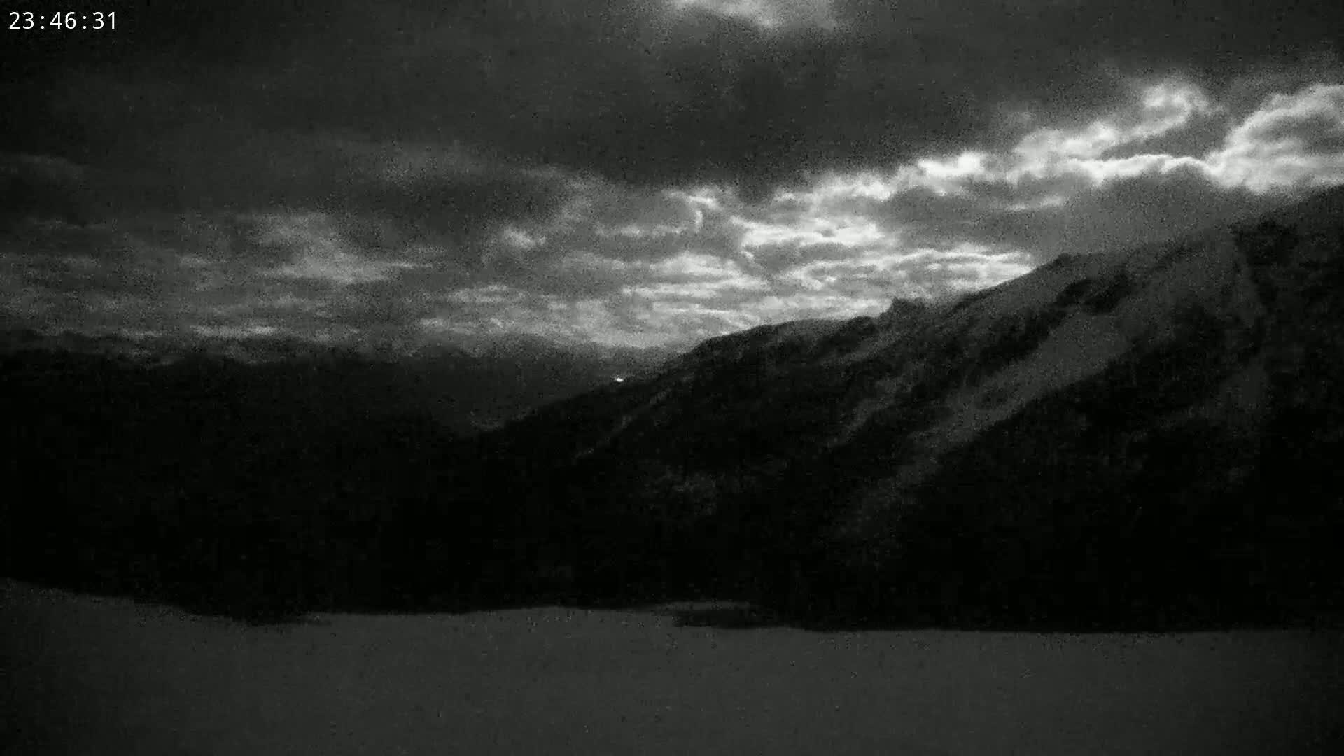 A nighttime view of a snow-covered mountain range under a cloudy sky.