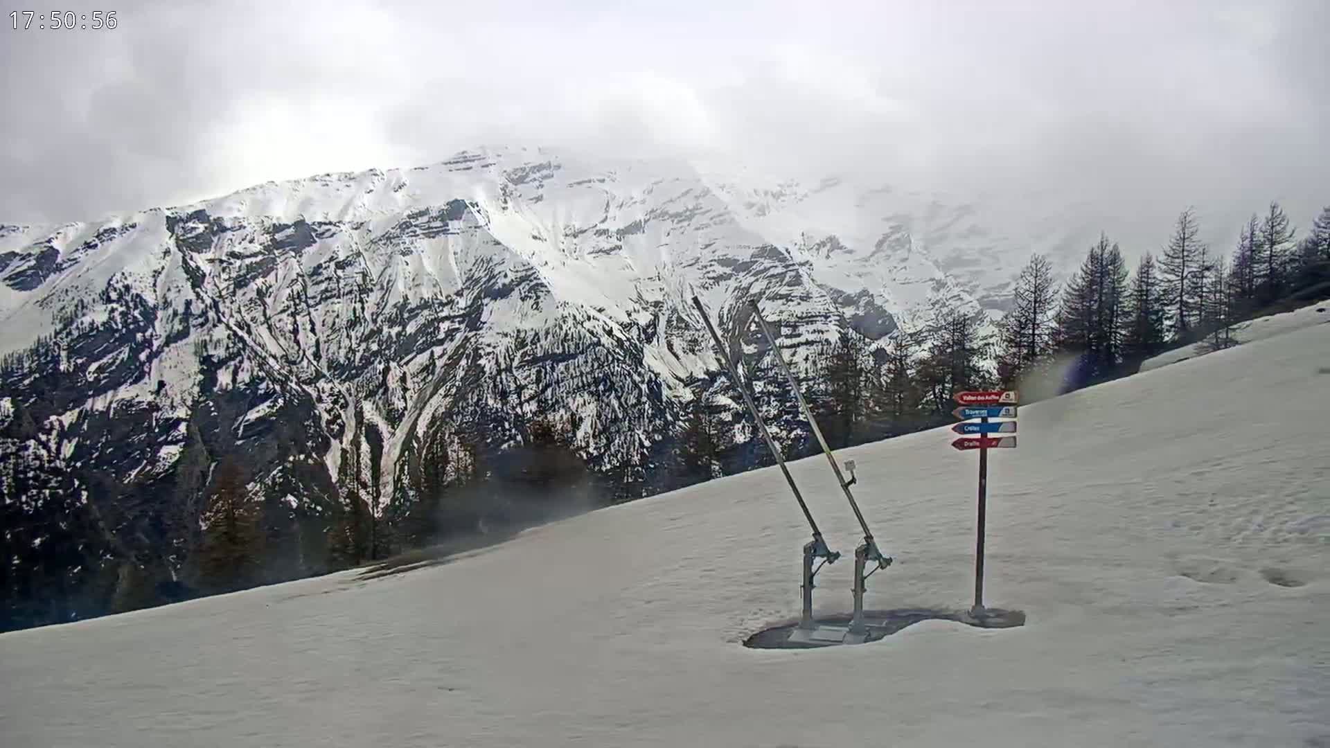 A ski lift sits on a snow-covered hillside overlooking a snow-capped mountain range under an overcast sky.