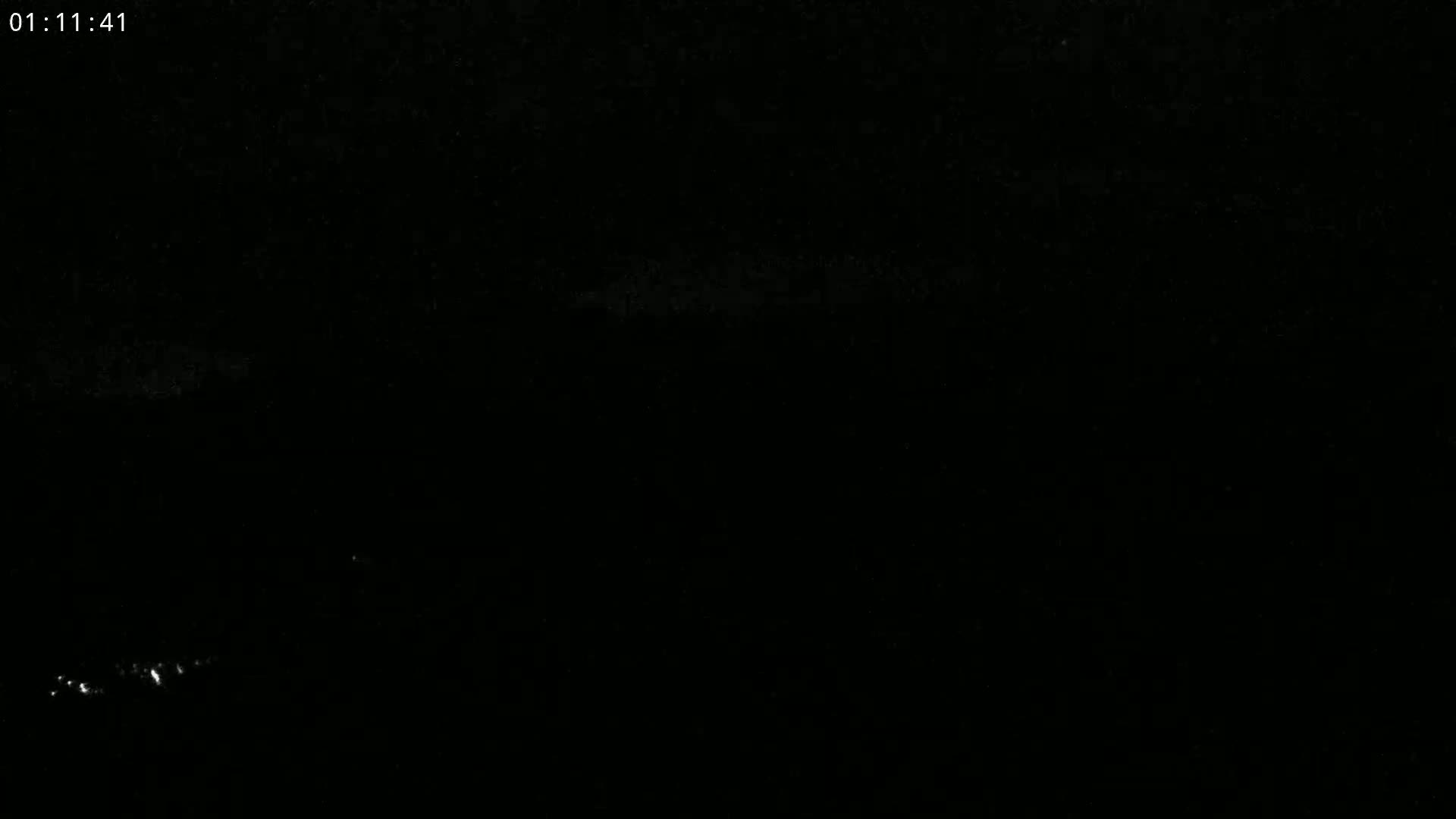 A nighttime, low-light image shows a faint line of lights on the horizon.