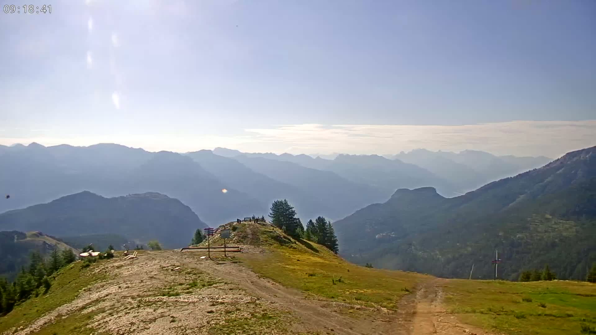 A mountaintop vista reveals a hazy, sunny day with a view of distant mountain ranges.