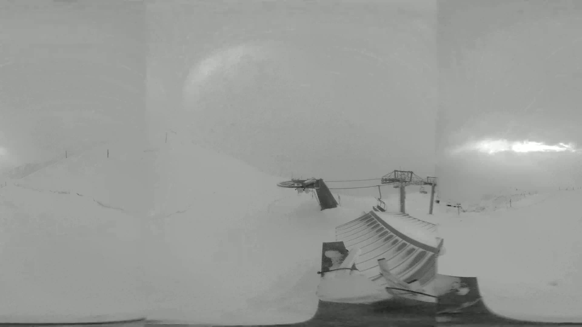 A snow-covered ski lift and surrounding slopes are visible in a heavy snowstorm.