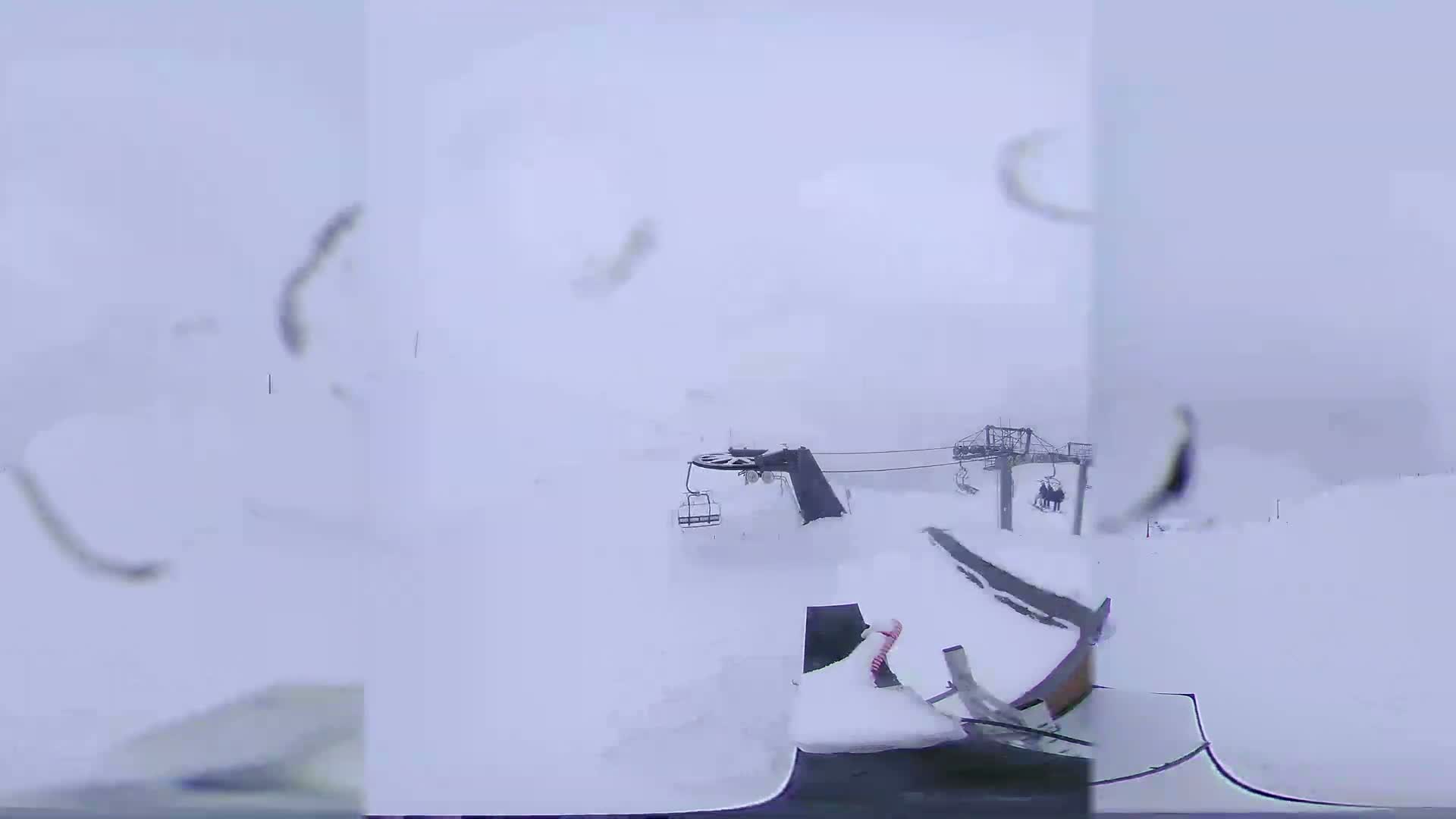 A snow-covered ski lift and a snow-covered vehicle are visible in a heavy snowstorm.