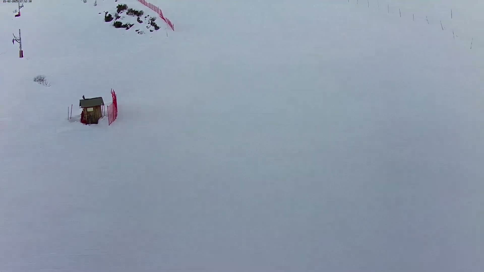 A small, wooden structure sits partially buried in snow on a mostly-empty snowy slope.