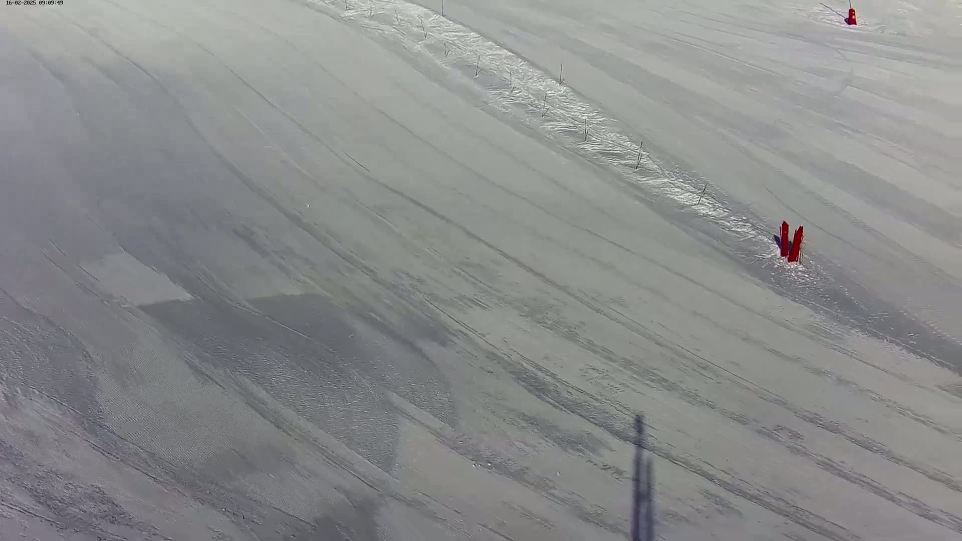 A high-angle view of a snow-covered ski slope with groomed runs and a few red markers.