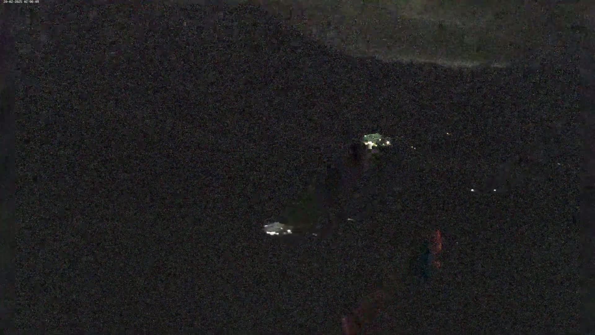 A nighttime, low-light image shows a dark, indistinct area with a few faint lights visible in the distance.