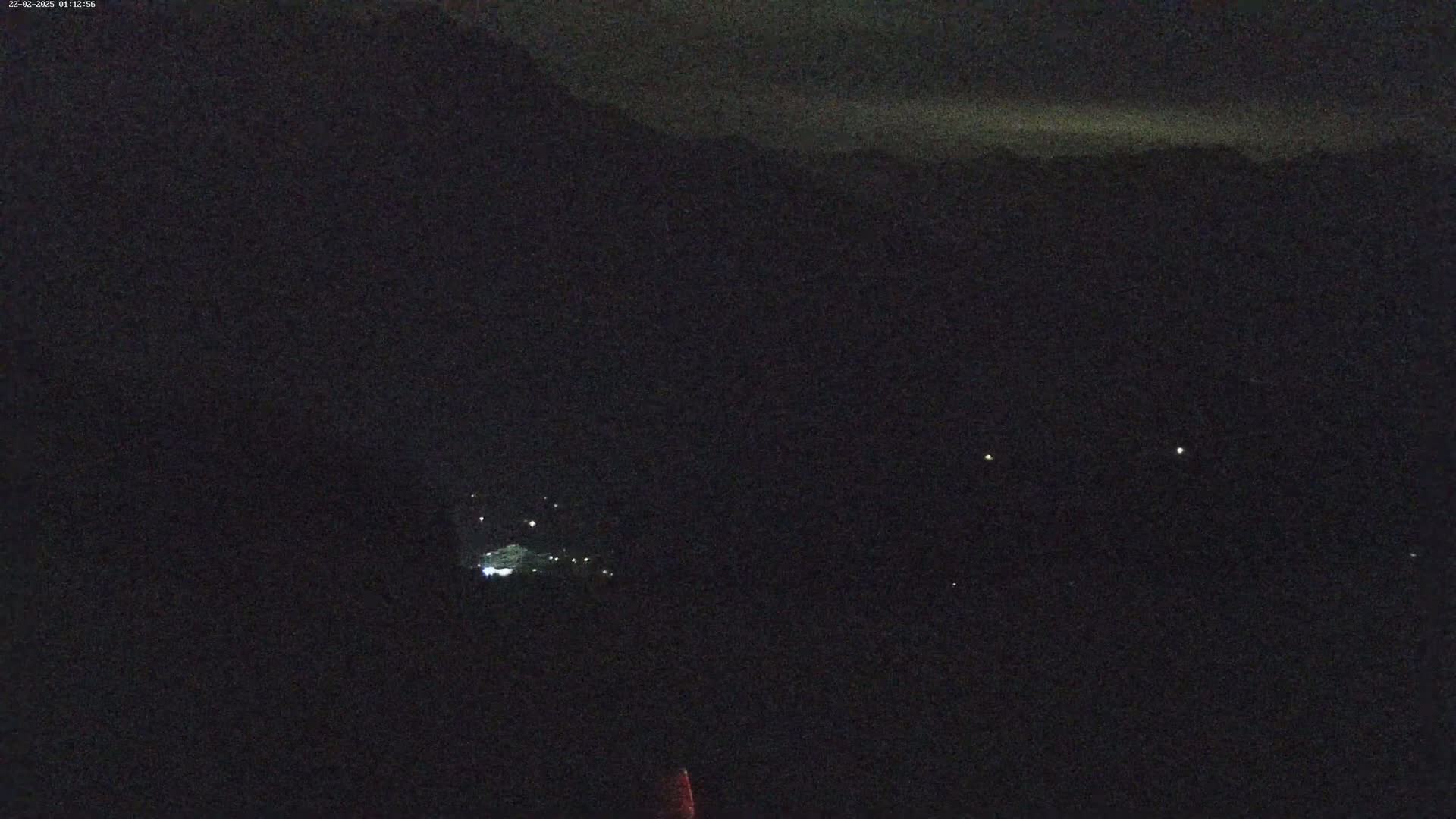 A nighttime long shot shows a dark, mountainous landscape with a few faint lights in the distance under a mostly clear sky.