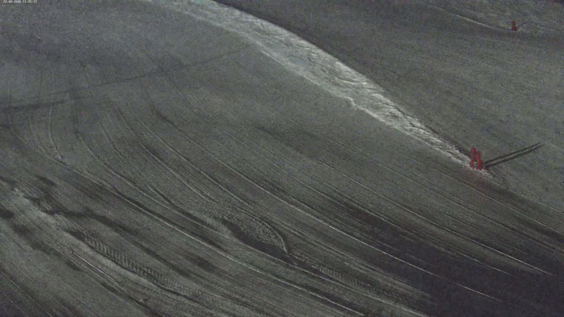 A dark gray surface with diagonal lines shows streaks of lighter gray, possibly from water or snow, and has small red objects near the bottom right.