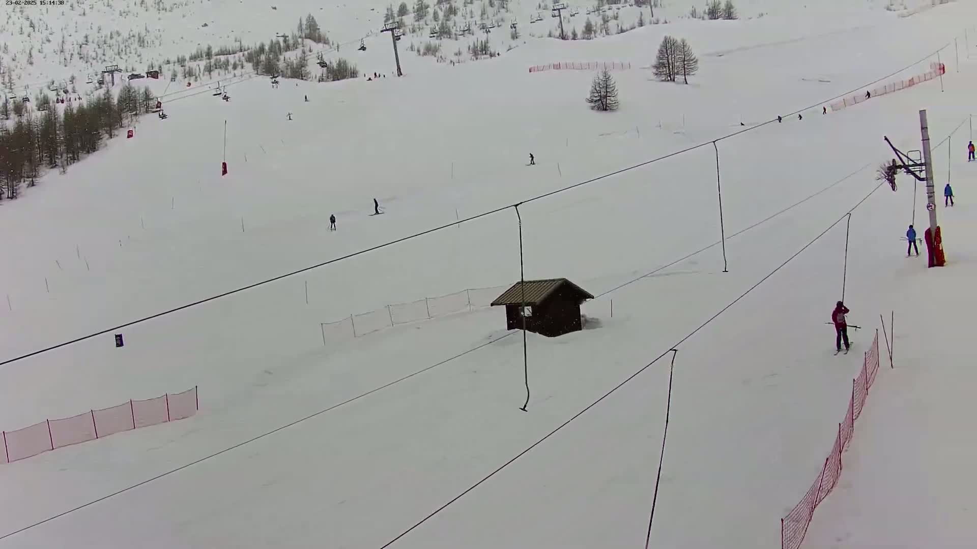 A mostly empty snow-covered ski slope with several skiers and a ski lift, under overcast skies.