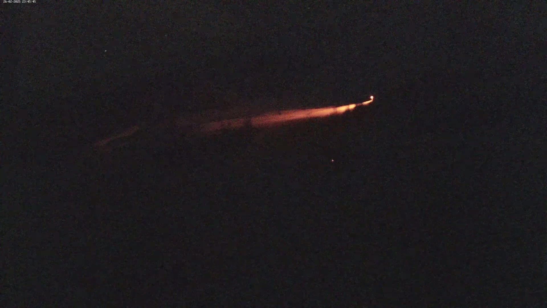 A long, thin, orange streak of light is visible against a dark, nighttime sky.