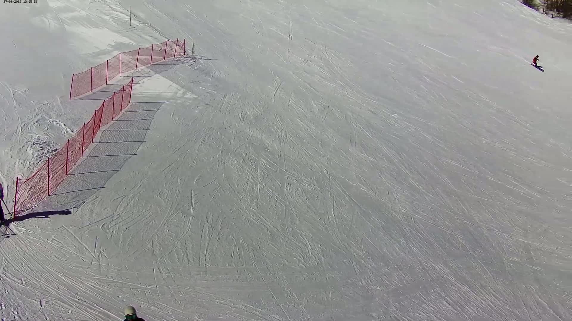 A snowy ski slope with a red safety net and several skiers.