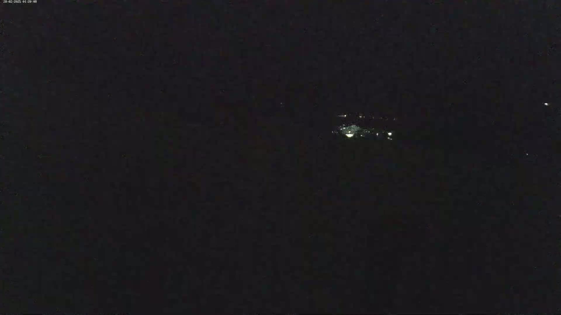A dark nighttime scene shows a small cluster of faint lights in the distance.