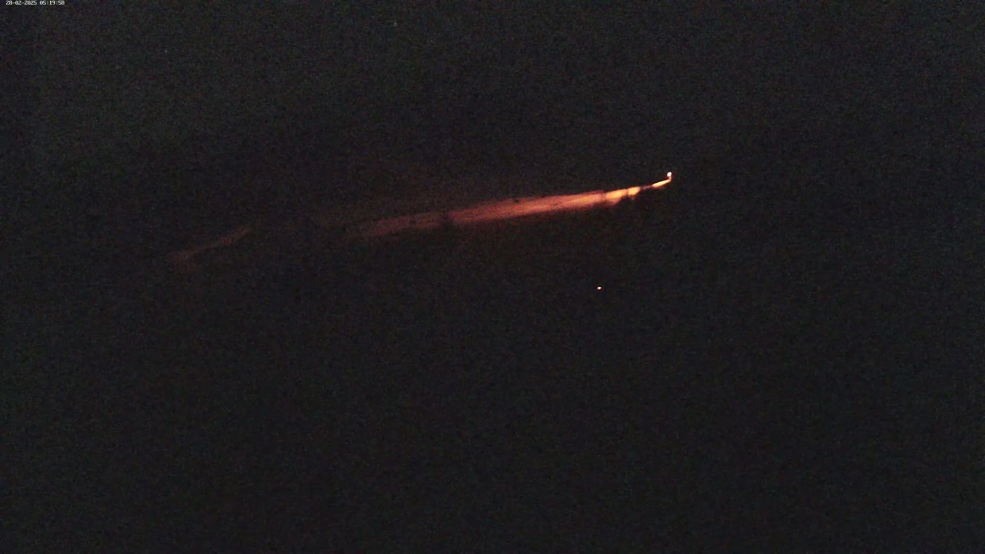A low-light image shows a long, thin, orange streak of light across a dark, nighttime sky.