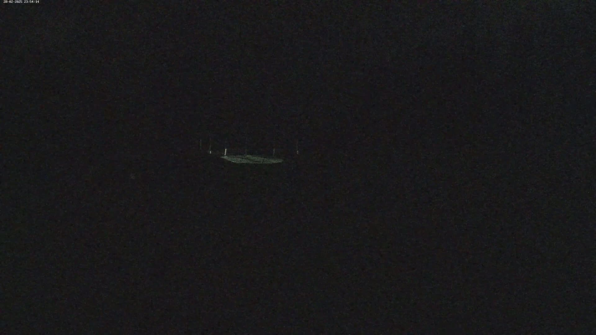 A dimly lit, dark area is visible at night, with a faintly illuminated flat surface possibly a road or field in the center.