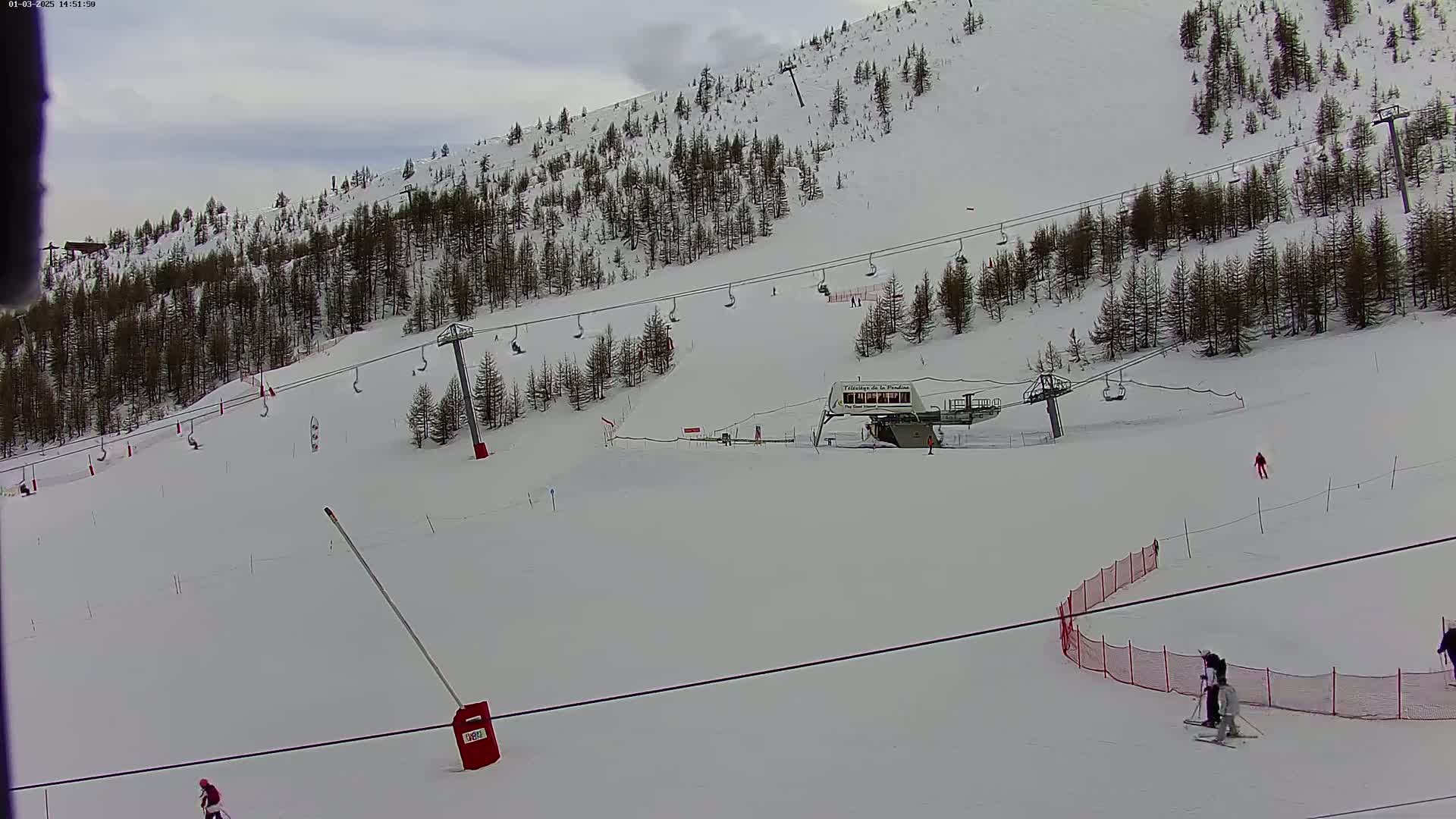 A snowy ski slope with several chairlifts, skiers, and a ski lift building under an overcast sky.
