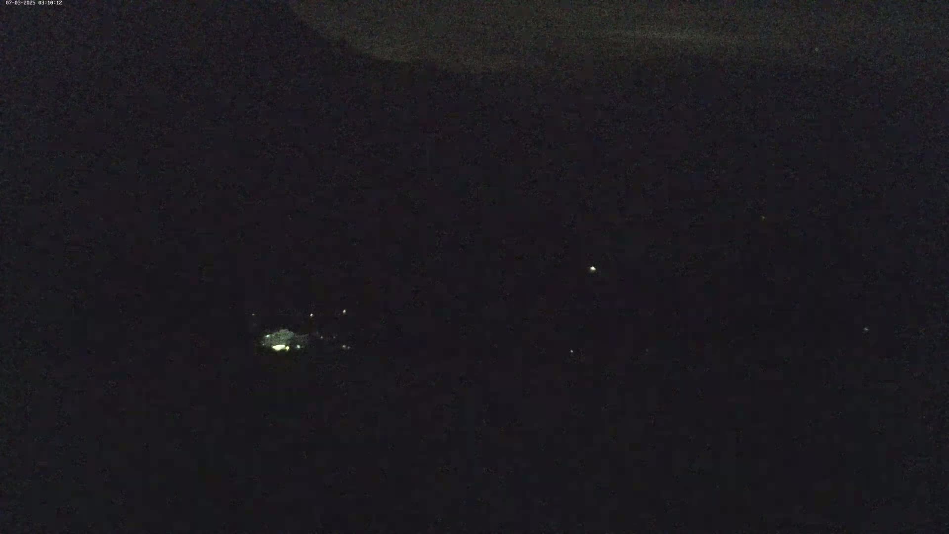 A nighttime long shot shows a few faint lights in the distance below a dark sky.