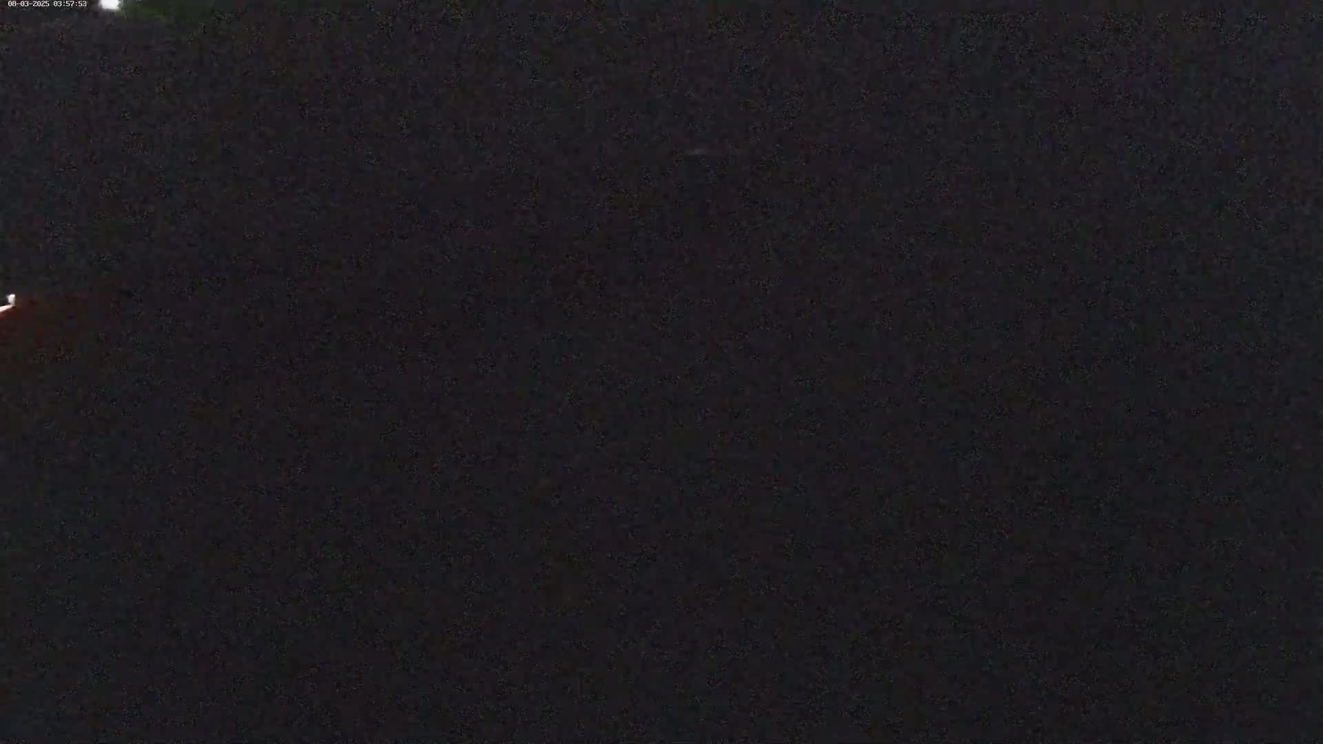 A mostly dark image shows a faint, reddish light in the upper left corner against a night sky.