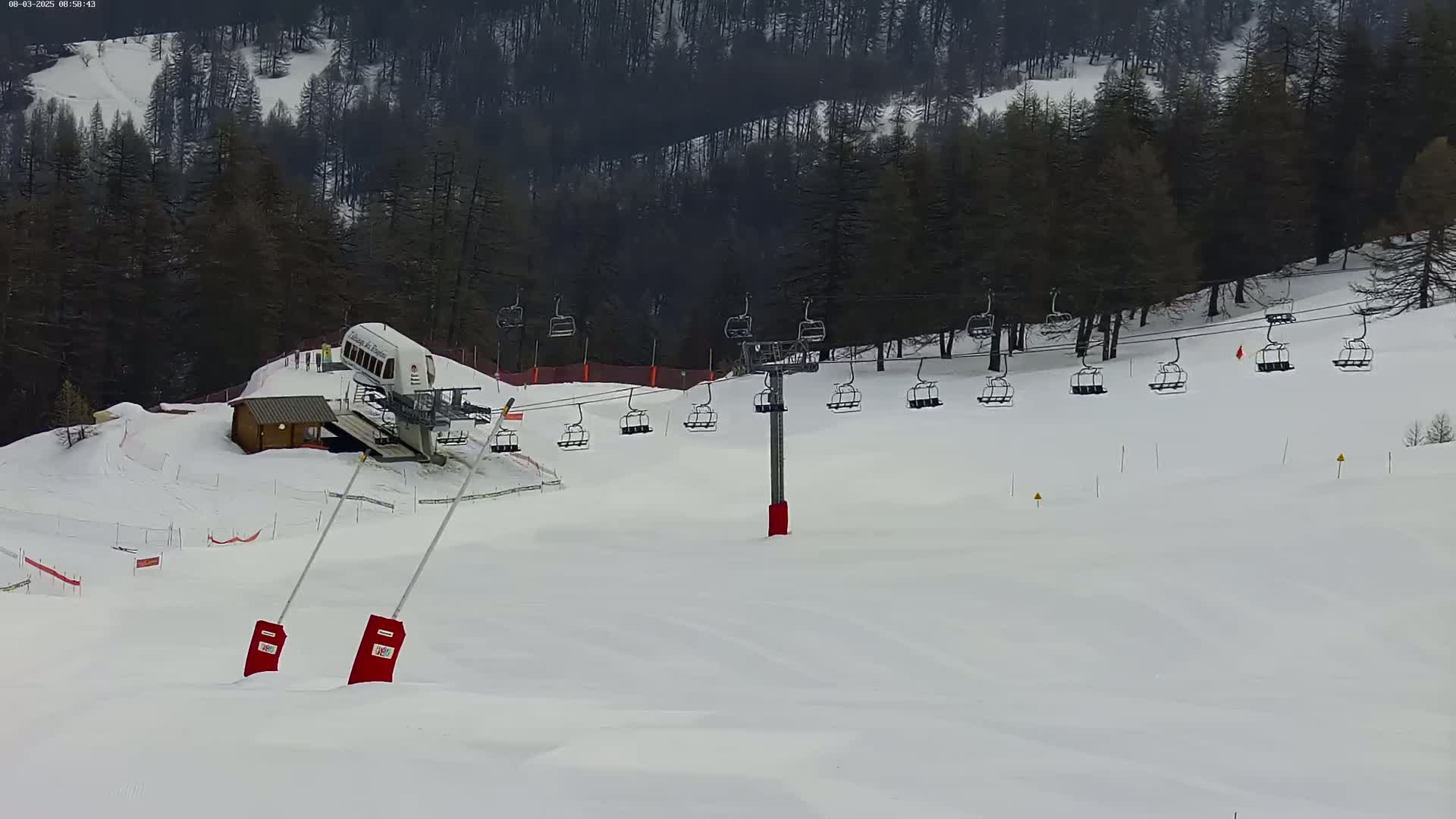 A chairlift ascends a snow-covered ski slope surrounded by dark evergreen trees under an overcast sky.