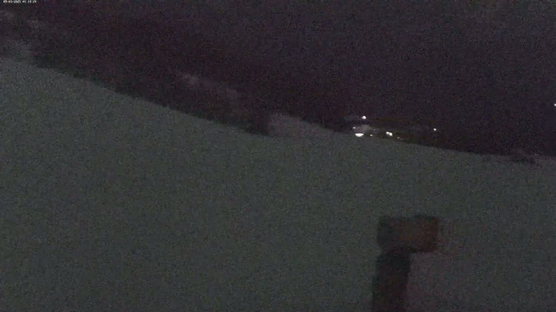 A nighttime, snow-covered slope is visible, with a few distant lights and a dark object in the foreground.