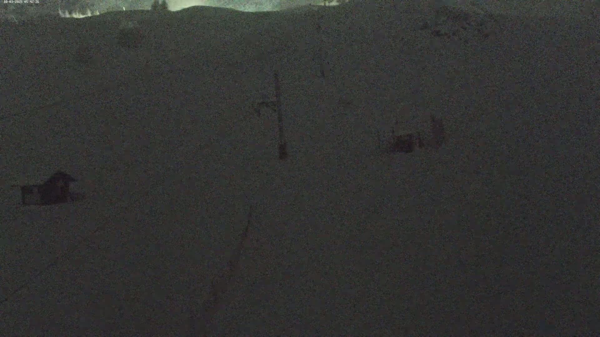 A dark, snow-covered landscape is visible at night, with a few indistinct structures and a ski lift in the distance.