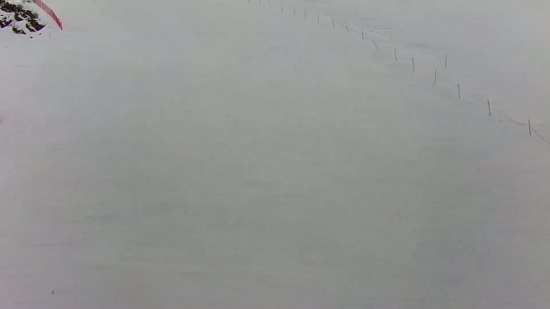 A snow-covered slope with a line of markers stretches diagonally across it under overcast skies.