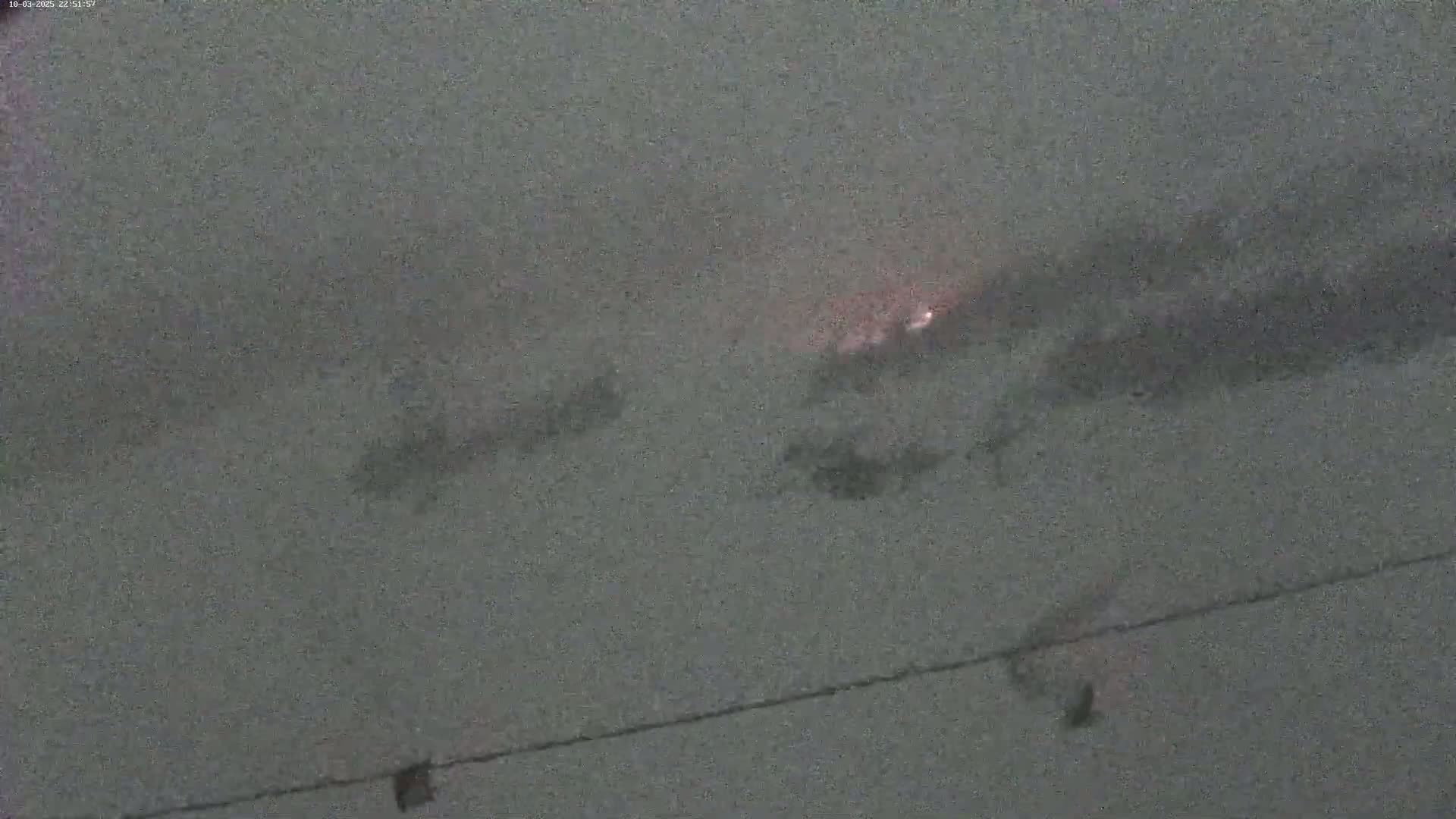 A blurry, nighttime image shows a faint orange glow in the distance under an overcast sky.