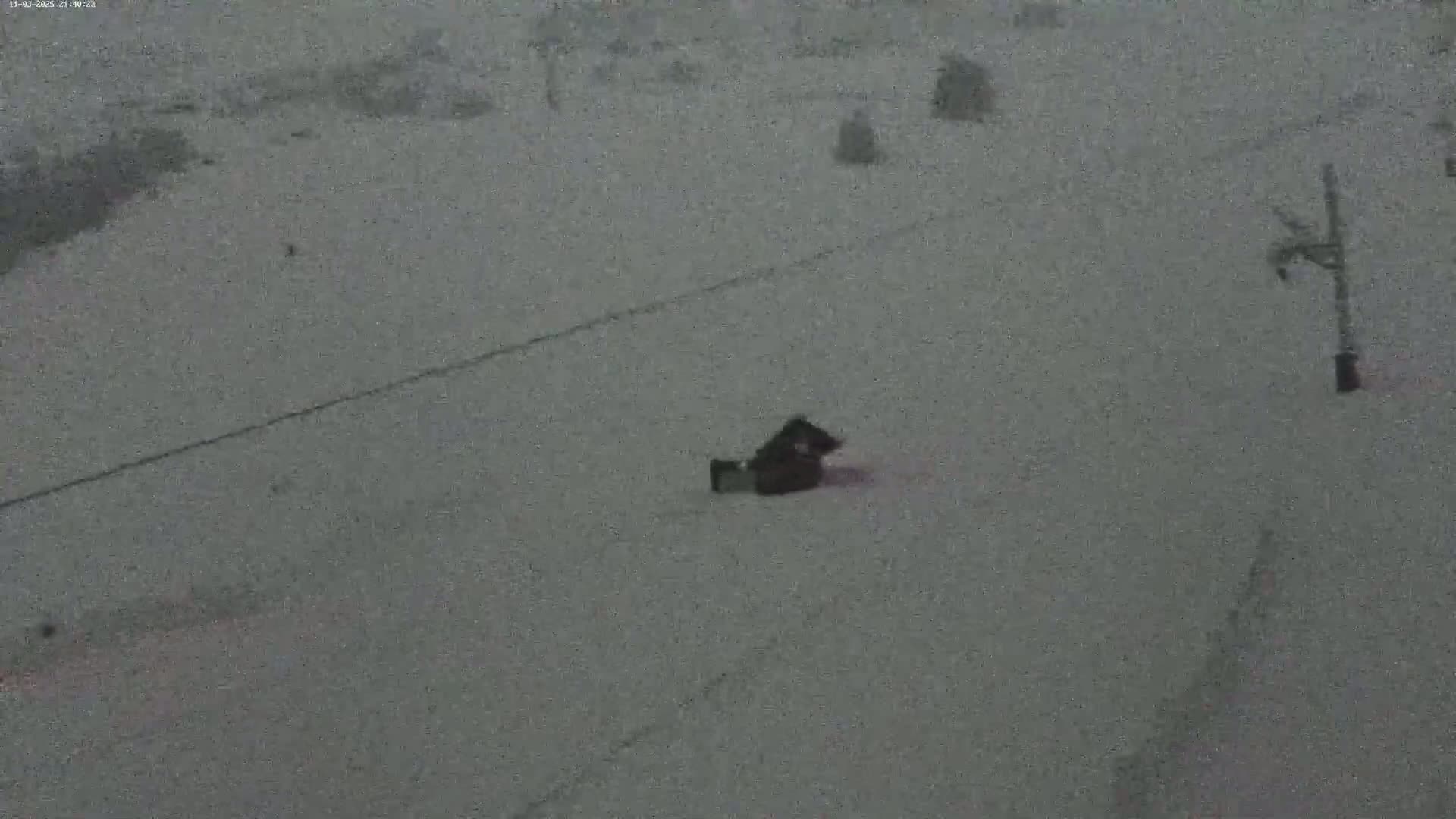 A snow-covered ground is seen with a dark object lying on it near a ski lift in snowy conditions.