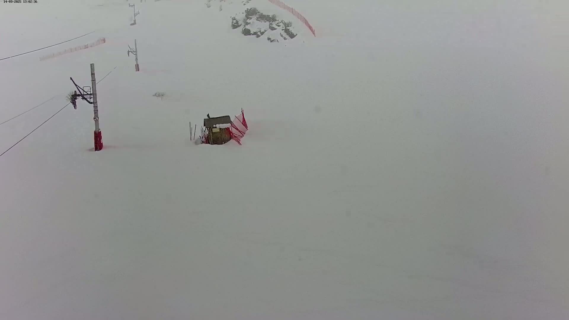 A snow-covered ski slope with a small structure and ski lift in the distance during a heavy snowstorm.
