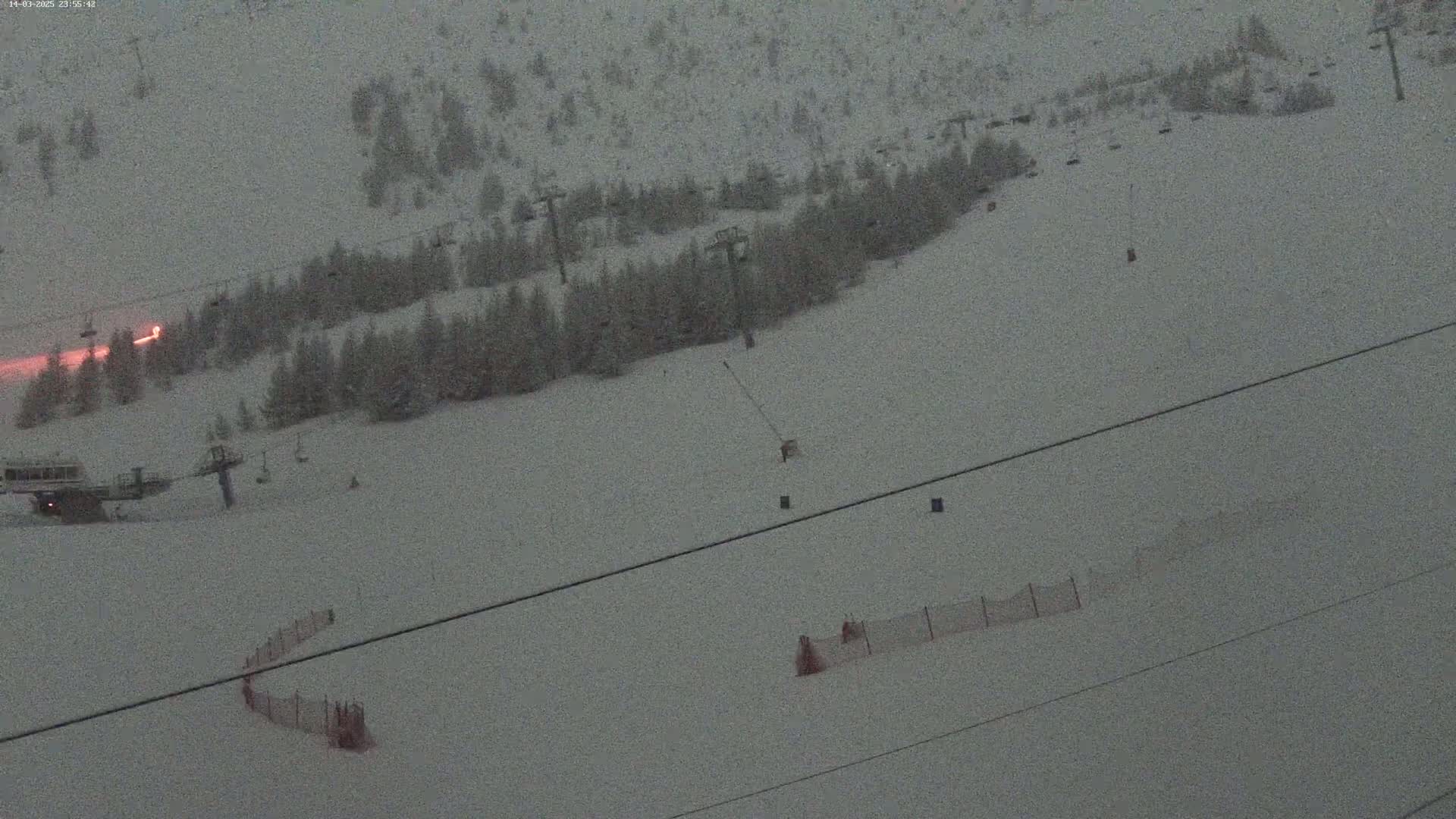 A snow-covered ski slope with chairlifts, sparsely populated with skiers, is visible under a twilight sky.