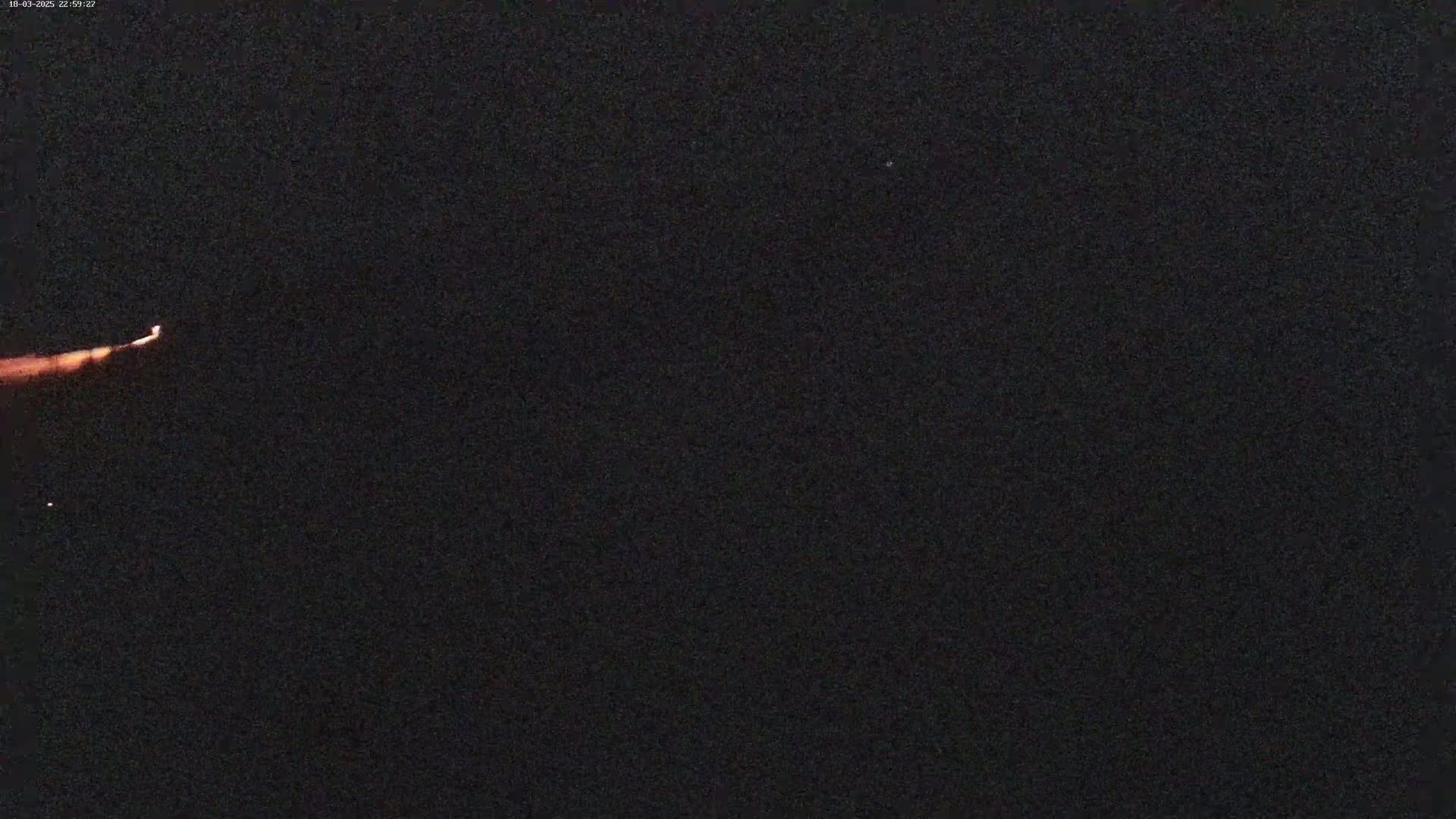 A low-light outdoor image shows a small orange light streak across a mostly black night sky.
