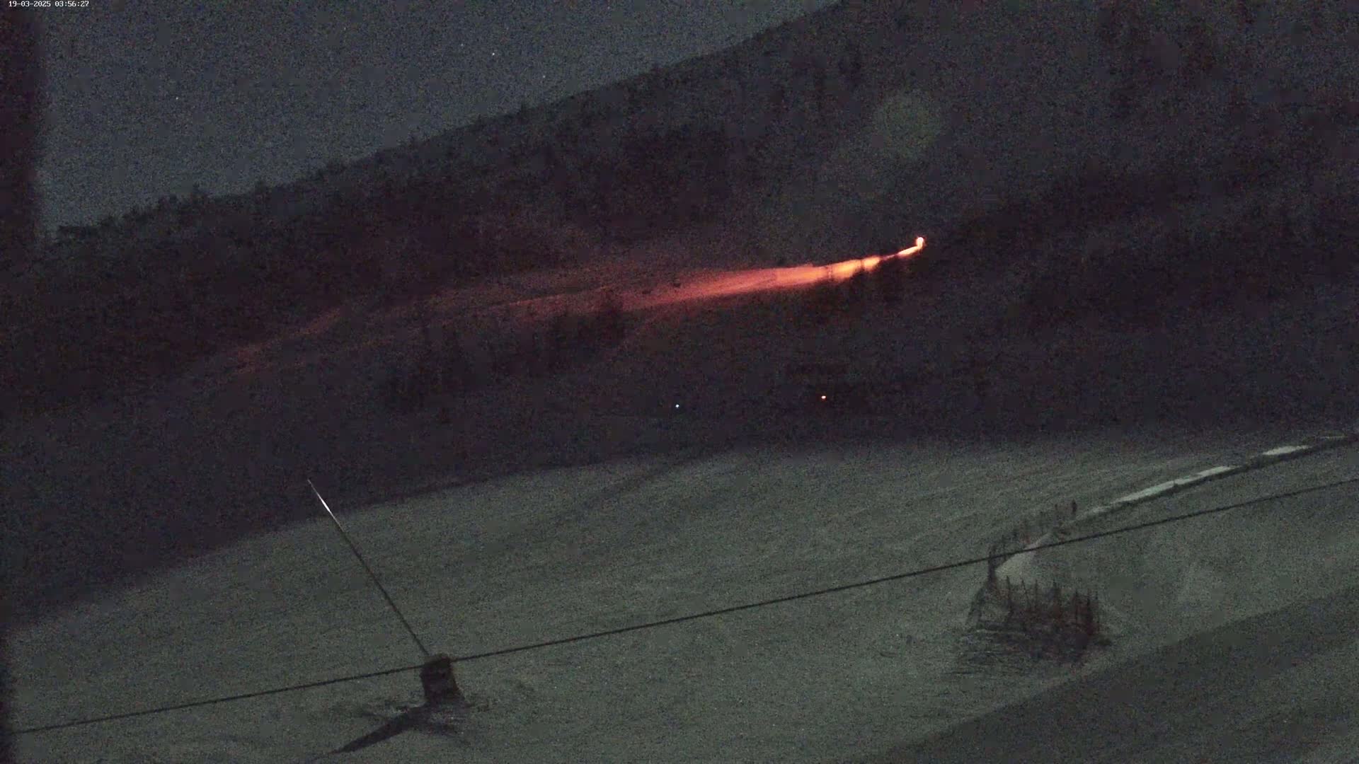 A long, glowing red streak is visible on a dark, snowy hillside at night.