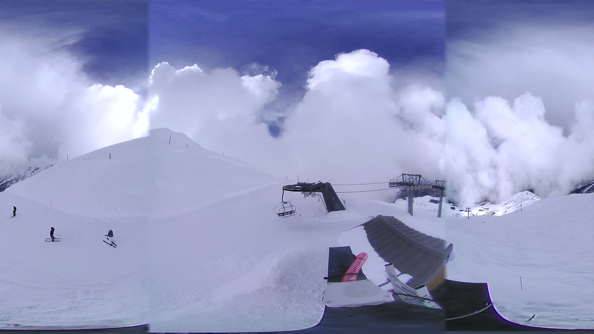 A snowy mountain slope with a chairlift and several skiers under a partly cloudy sky.