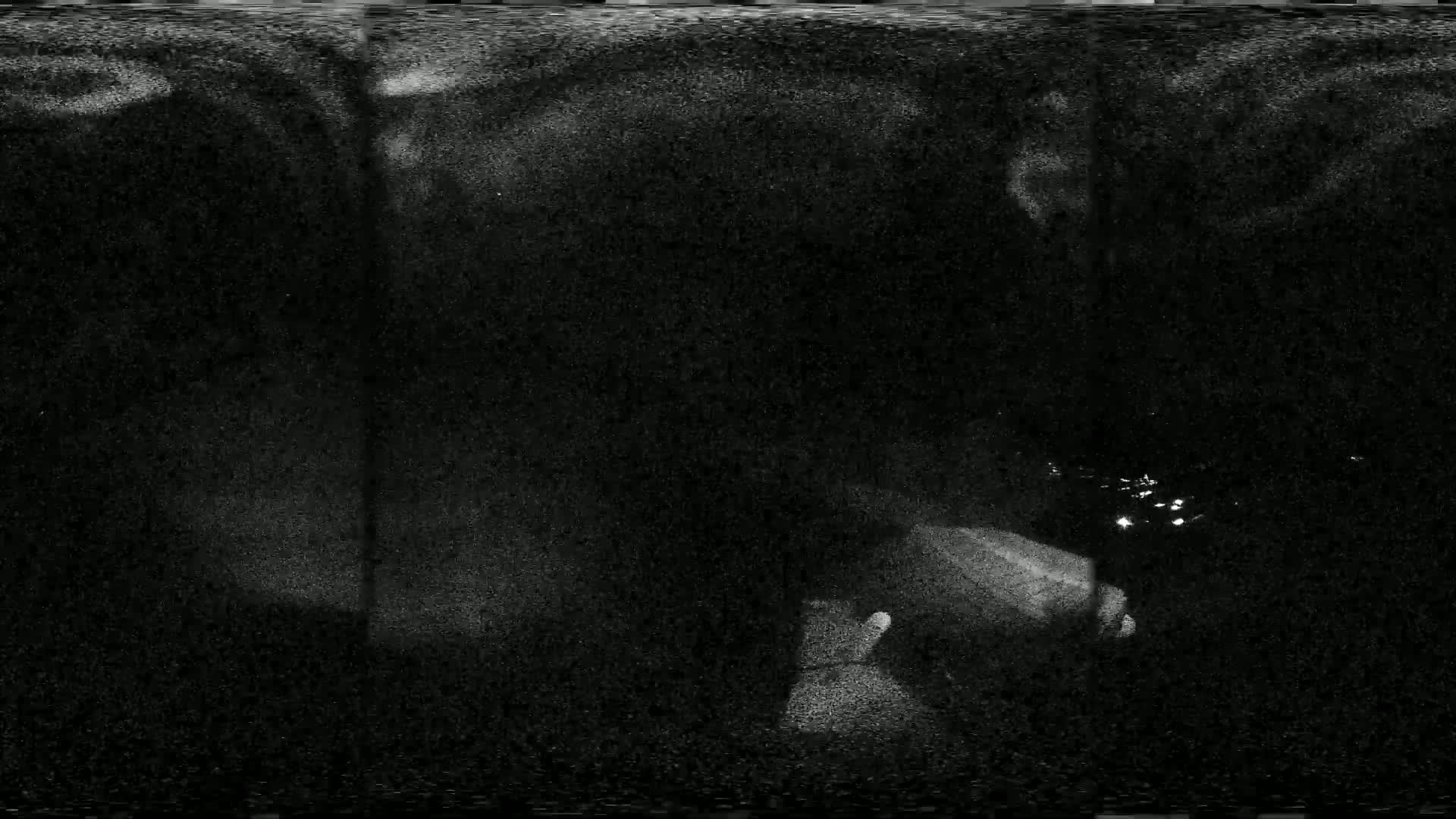 A grainy, low-light image shows indistinct shapes and possibly some water reflecting light in the bottom right corner.