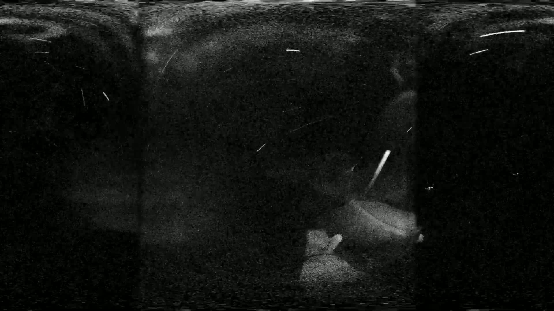 A blurry, grainy black and white image shows a dark, possibly nighttime scene with streaks of light possibly from falling snow or rain.