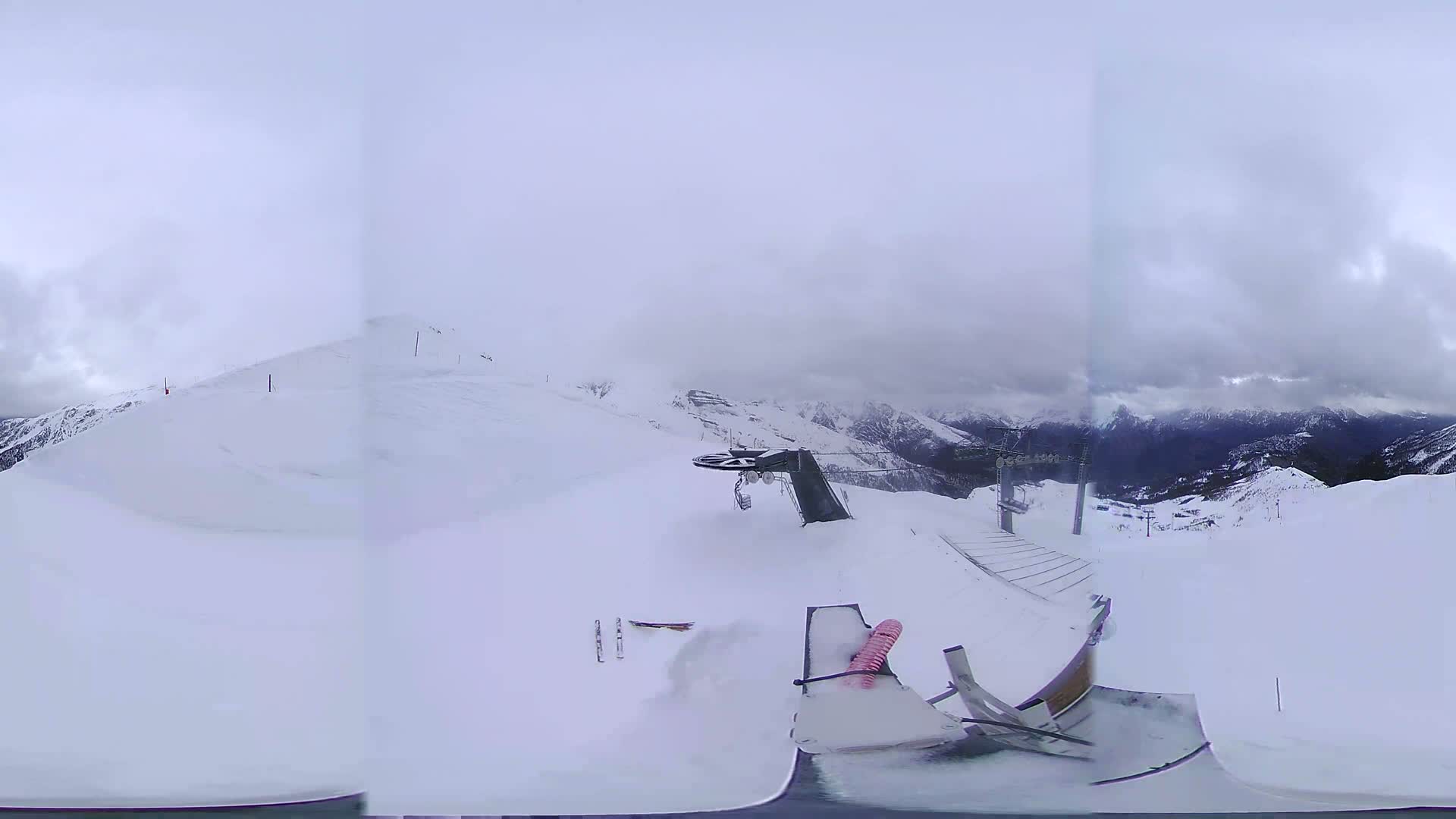 A snowy mountaintop view shows a ski lift and a snow-covered landscape under an overcast sky.