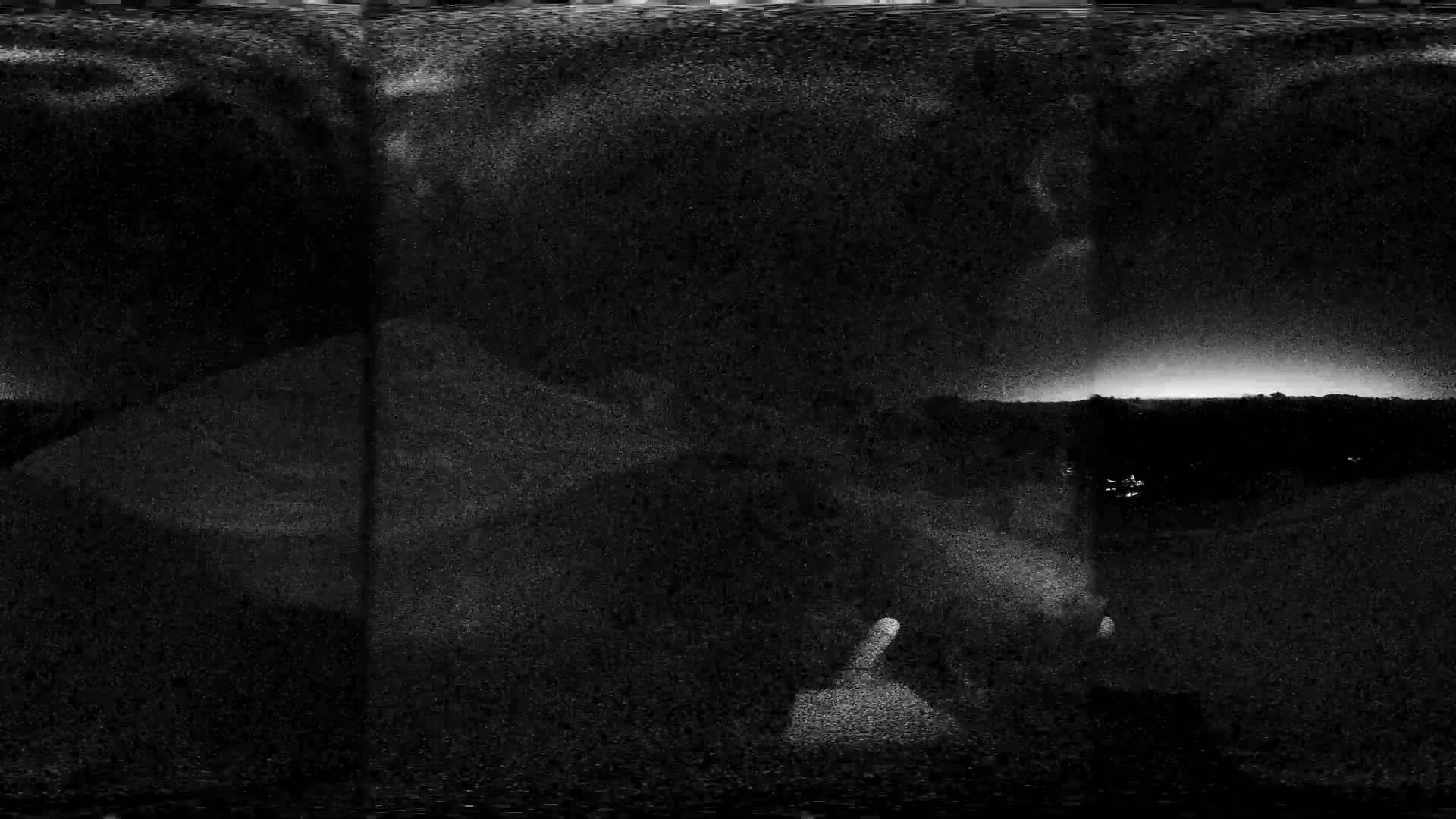 A grainy, nighttime image shows a dark landscape with a faint, light horizon, possibly a sunset or sunrise.