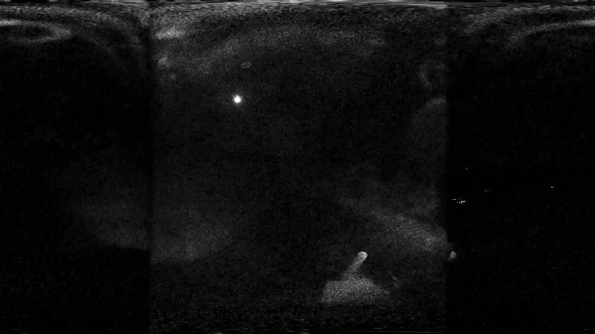 A grainy, dark image shows a bright light in the center, surrounded by a speckled, possibly snowy or dusty, night sky.
