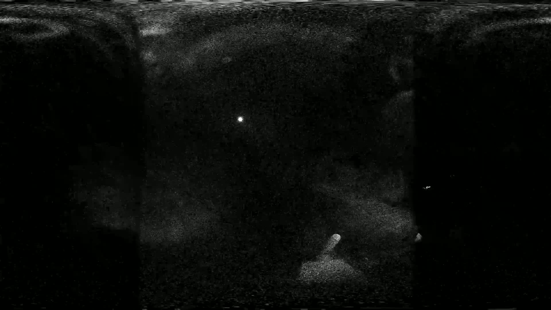 A grainy, dark image shows a bright light in the center and fainter lights near the bottom and right edges.