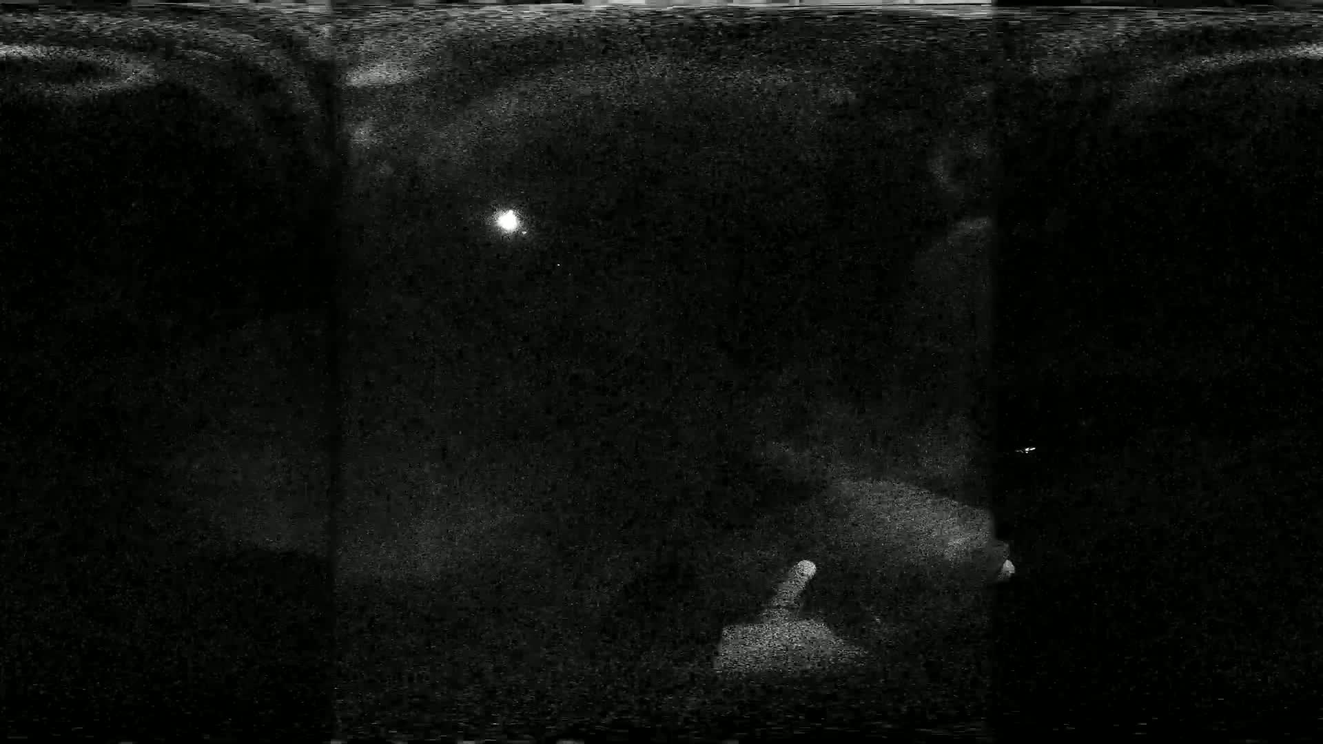 A grainy, dark image shows a faint light source in the center, possibly at night.