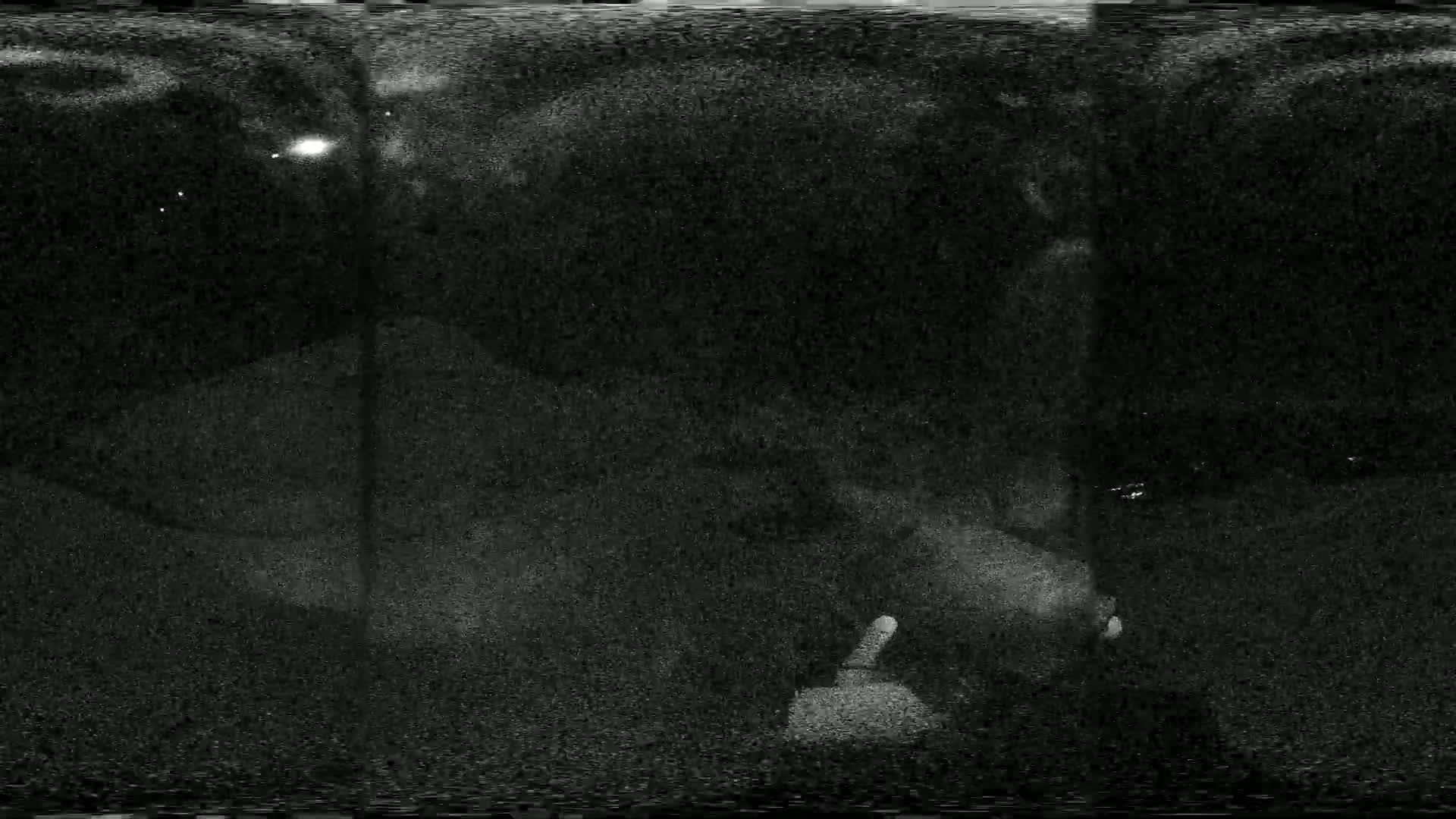 A grainy, low-light nighttime image shows a dark, indistinct area with a few distant lights.