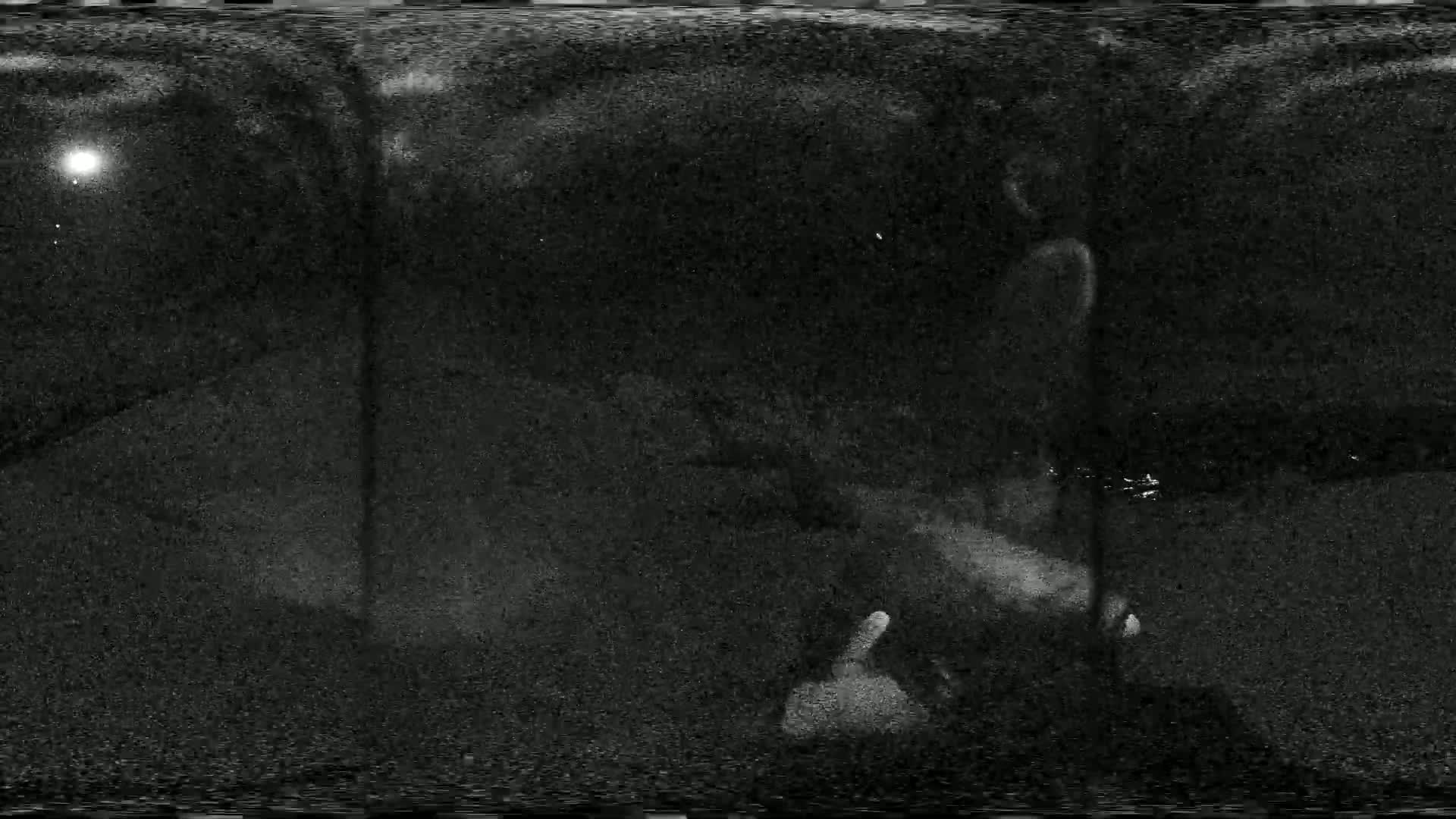 A grainy, low-light image shows two blurry figures in a dark, nighttime outdoor setting under a cloudy sky.