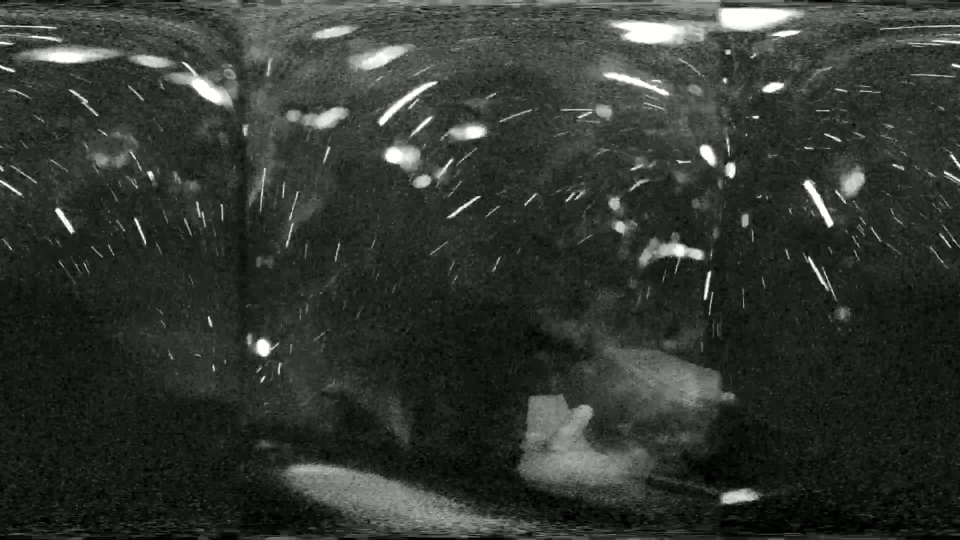 A nighttime, snowy scene is visible through a vehicle's windshield, with blurry lights and indistinct objects in the background.