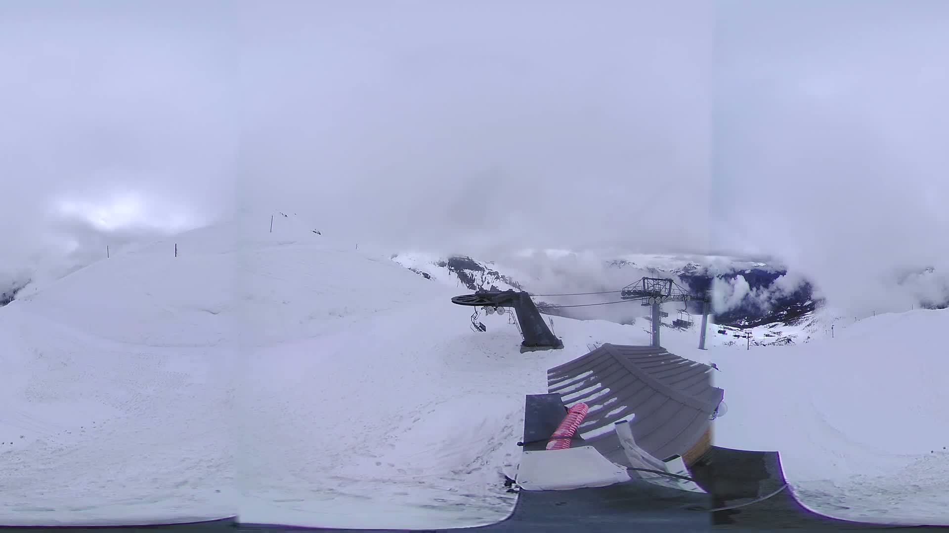 A snowy mountaintop scene with foggy weather shows a ski lift and a snow-covered slope.