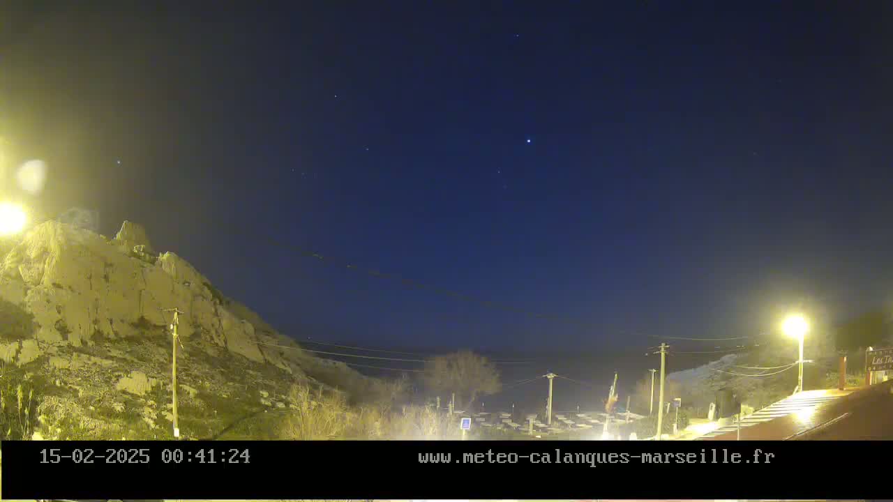 A nighttime view of a rocky hillside overlooking a calm body of water under a clear, starry sky.