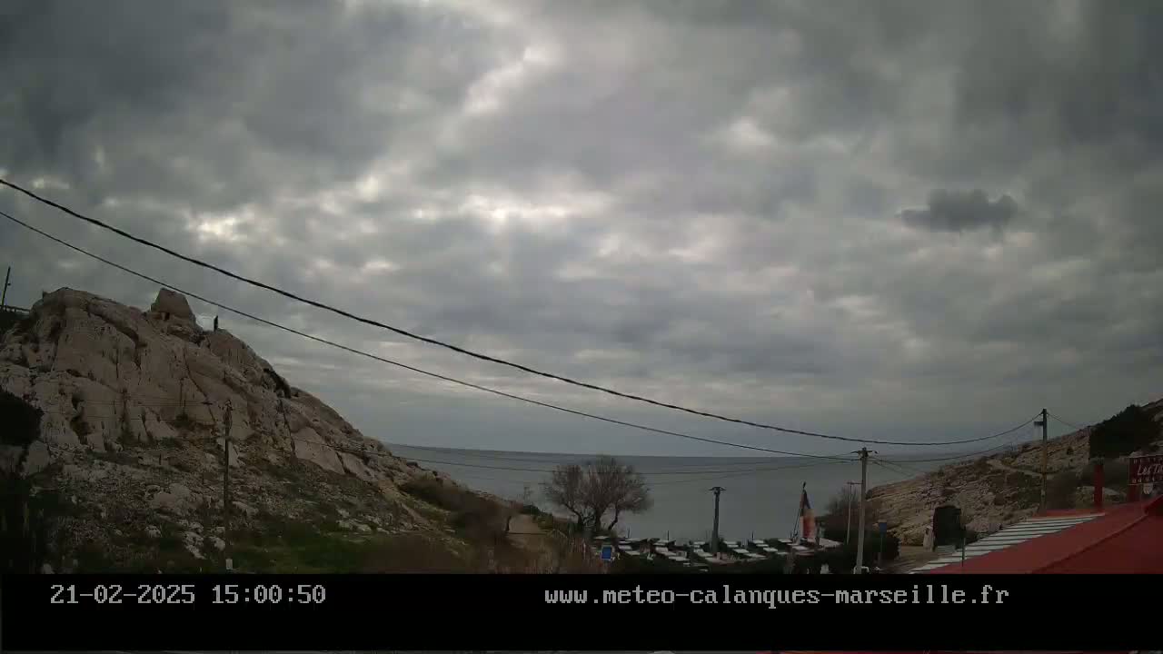 A rocky hillside overlooking a calm sea under a mostly cloudy sky.