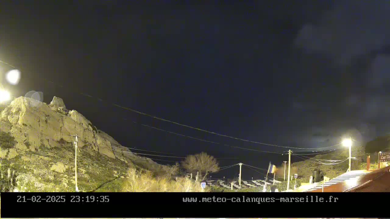 A nighttime view of a rocky hillside with sparse vegetation under a mostly clear, dark sky.